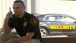 Security guard talking on radio with patrol car in background