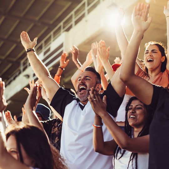 People in crowd cheering and clapping with arms raised